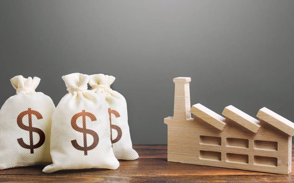 A wooden house and three money bags(dollar sign on it) placed on a wooden table with gray background.