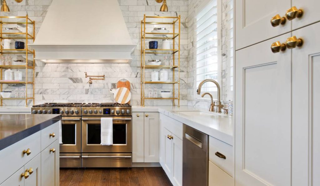 a kitchen with white cabinets, brass handles, metallic stove and wooden floors