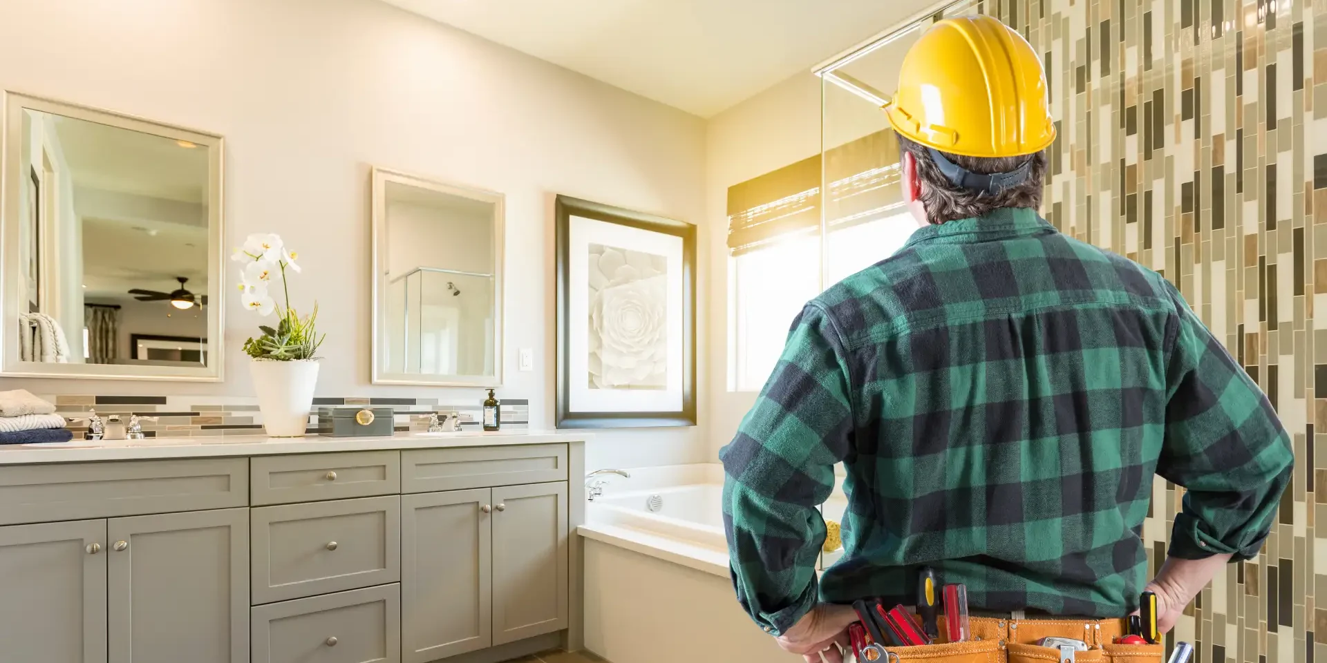 A home renovation contractor in a hard hat standing in front of a bathroom