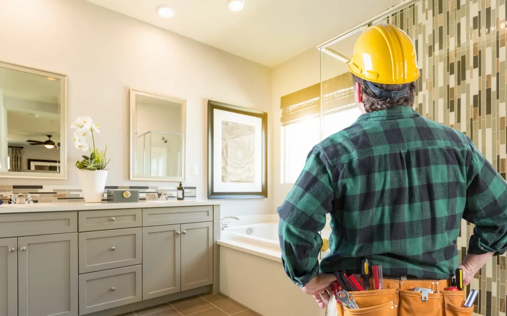 A home renovation contractor in a hard hat standing in front of a bathroom