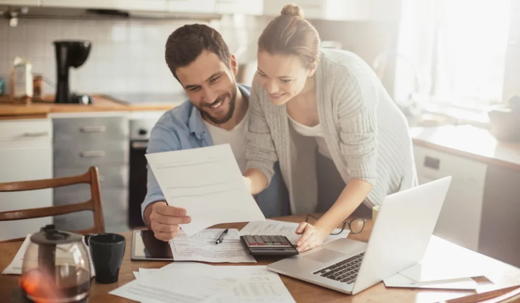 two people looking at a paper while a calculator and a laptop is placed on the table