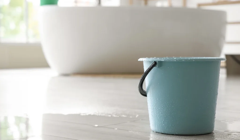 A blue bucket is placed under a leaky ceiling inside a bathroom