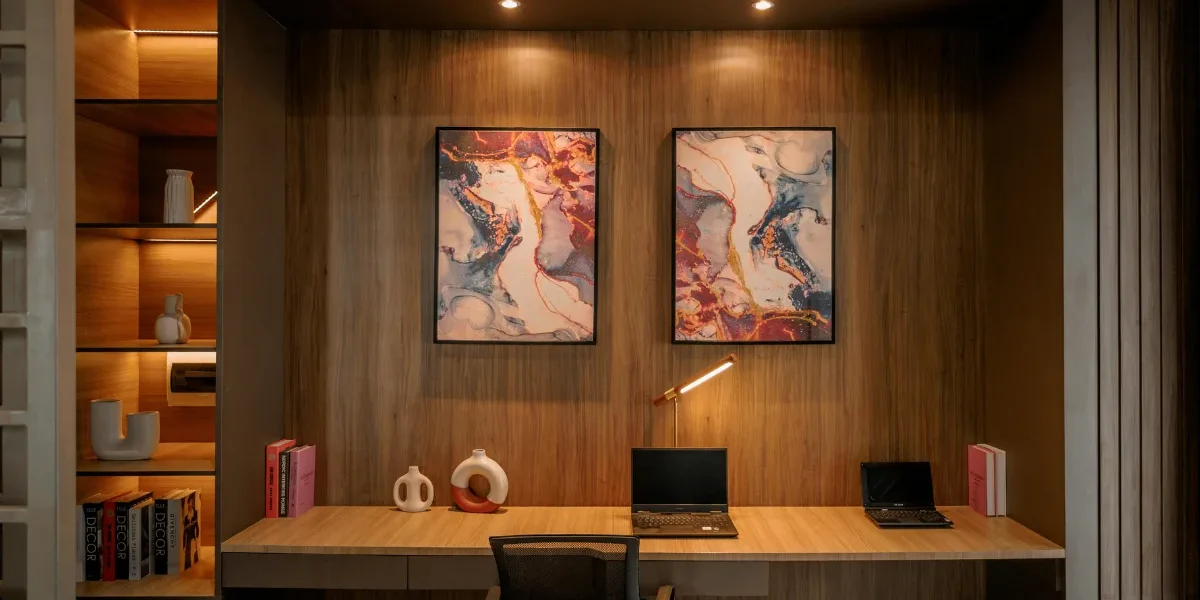 Modern home office with built in wooden shelving, warm lighting, minimalist desk setup, and abstract wall art.