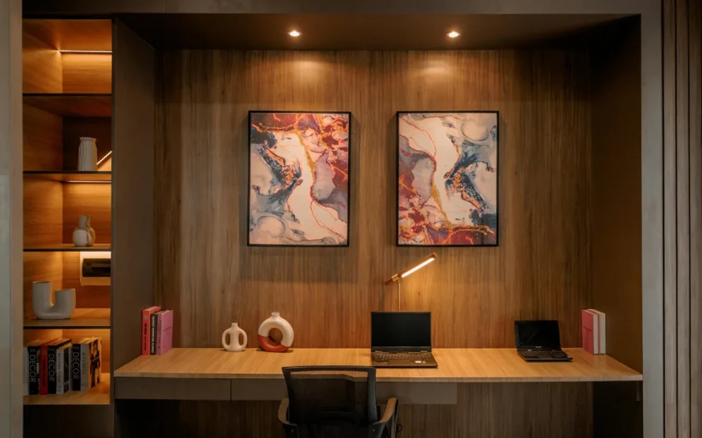 Modern home office with built in wooden shelving, warm lighting, minimalist desk setup, and abstract wall art.