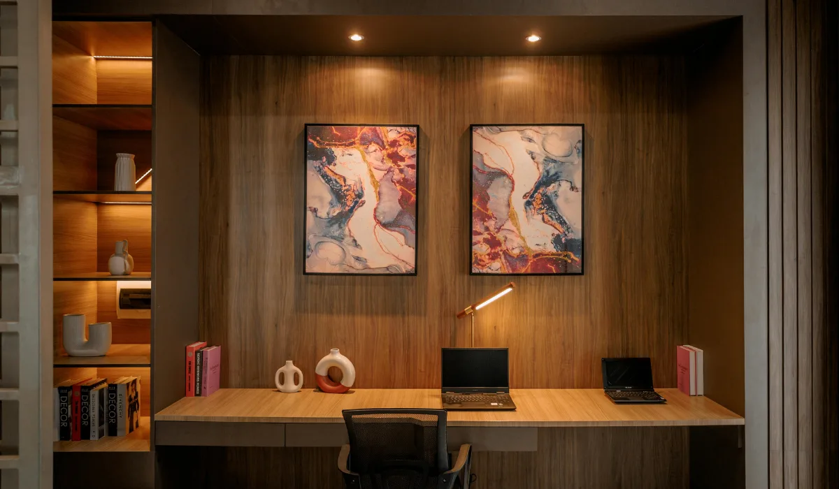 Modern home office with built in wooden shelving, warm lighting, minimalist desk setup, and abstract wall art.