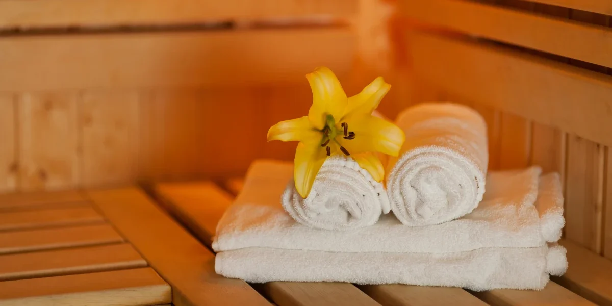 wellness-design-custom-homes-1 Rolled white towels with a yellow flower inside a warm wooden sauna inside the house.