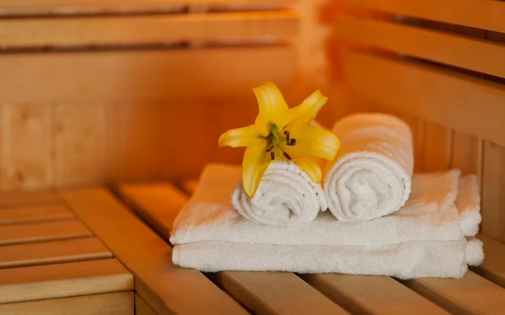 Rolled white towels with a yellow flower inside a warm wooden sauna inside the house.