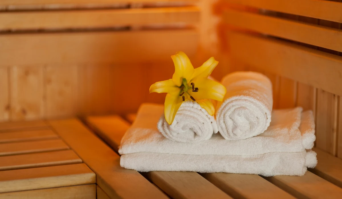 Rolled white towels with a yellow flower inside a warm wooden sauna inside the house.